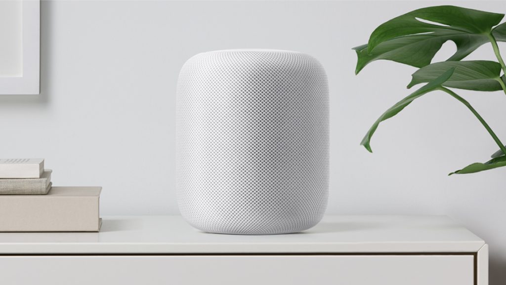 Original white HomePod beside books and a leafy plant